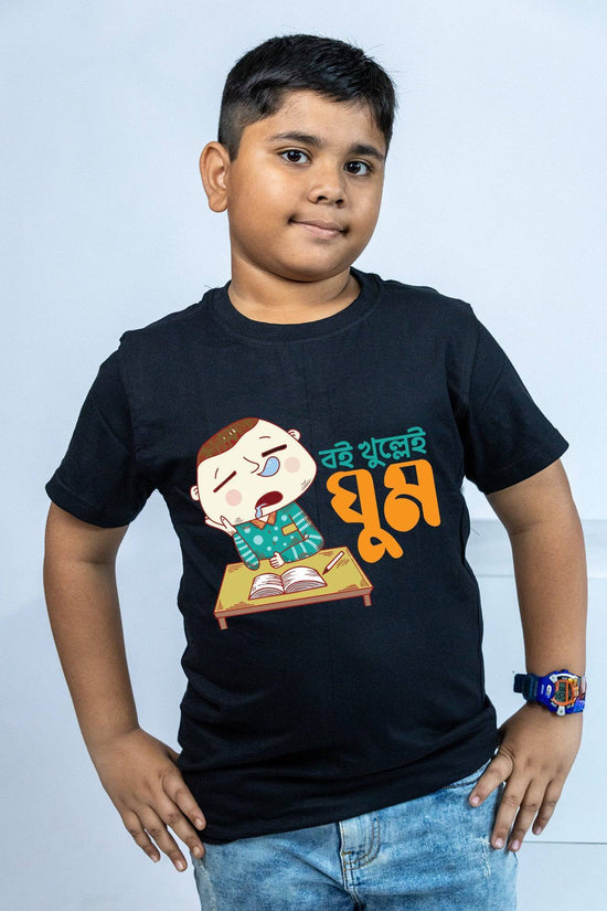 Bengali TShirt for kids featuring 'Boi Khulle i Ghum' text and a cartoon of a sleepy boy at a desk. Black cotton T-shirt, soft and breathable.