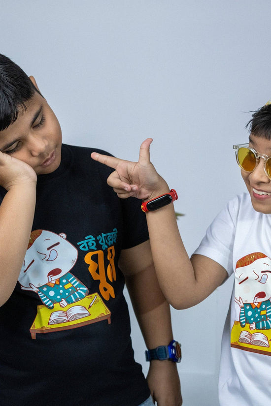 Two kids wearing 'Boi Khulle i Ghum' Bengali TShirts, one in black and one in white, featuring a funny cartoon design. Perfect for kids' casual wear.