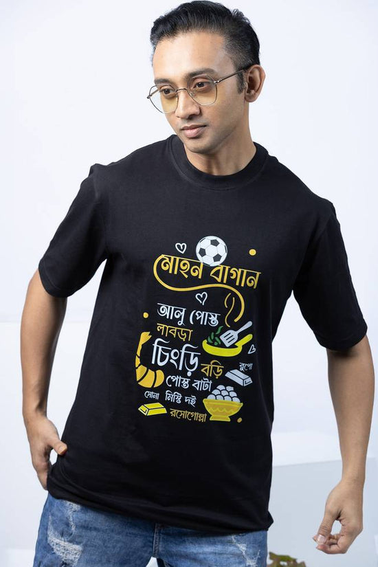 Ghoti-Kahini T-shirt featuring bold Bengali typography and doodle design on black fabric. A trendy Bangla fashion piece for casual wear.