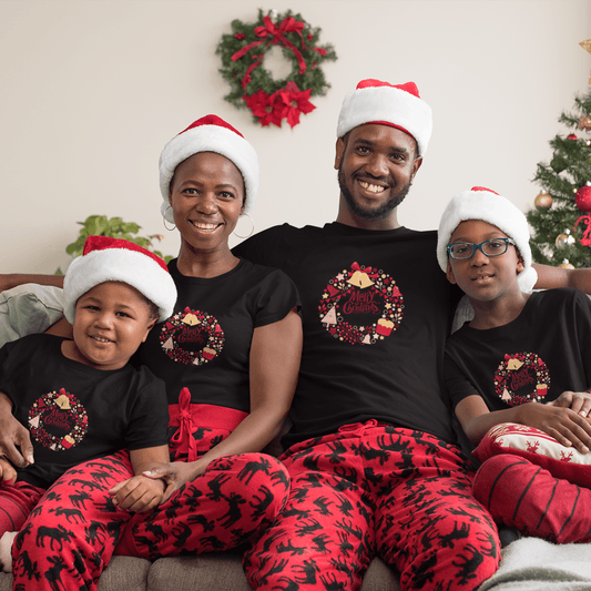 Family dressed in black unisex Christmas T-Shirts with festive designs, paired with red holiday-themed pants, sitting on a couch near a Christmas tree.