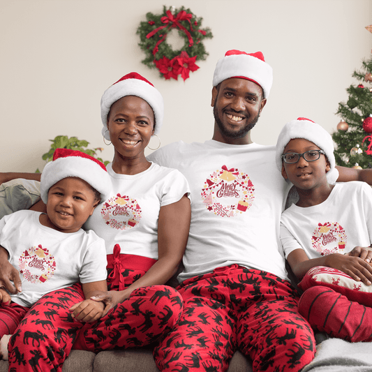 Family wearing unisex Christmas T-Shirts in white with festive designs, paired with red holiday-themed pants, sitting on a couch near a decorated Christmas tree.