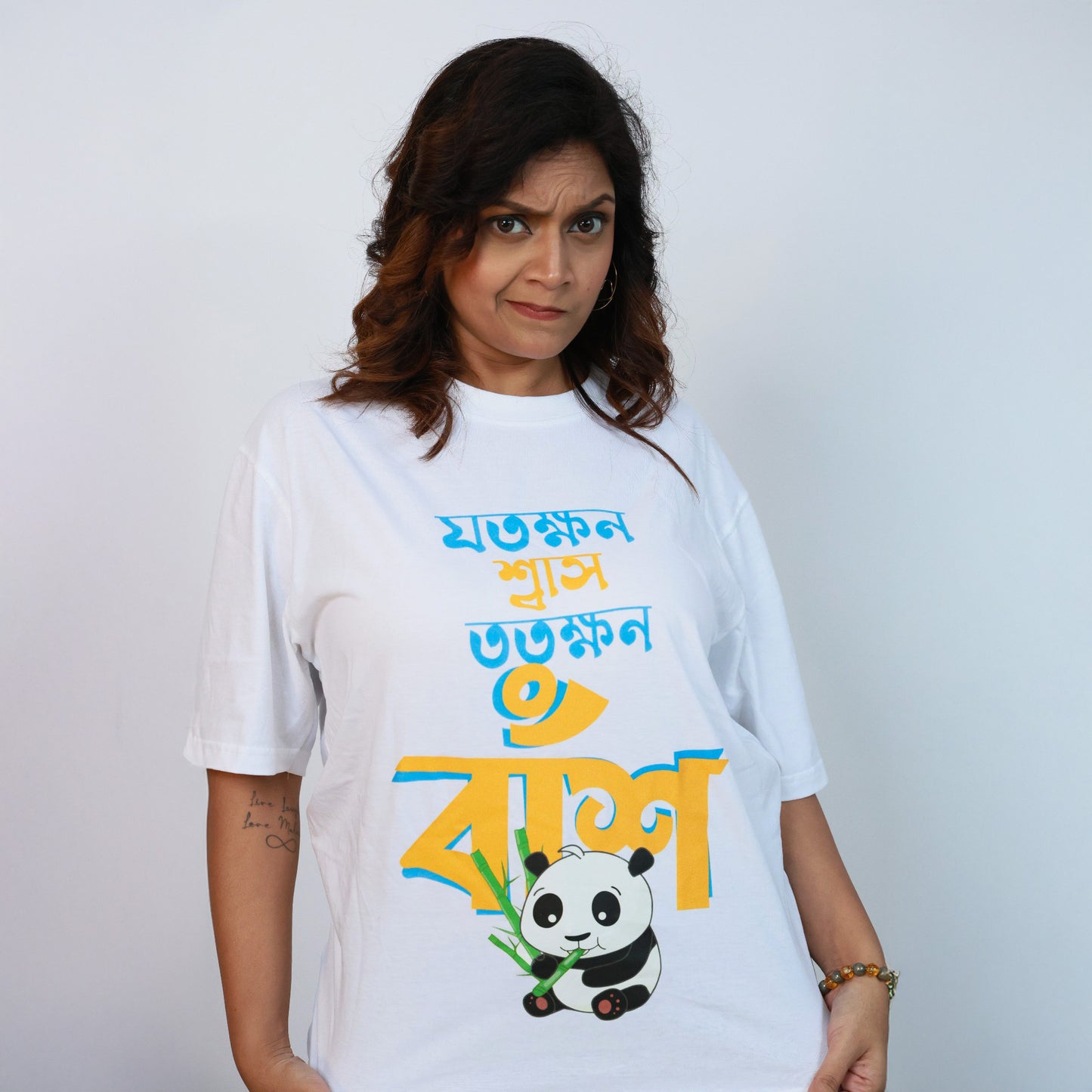 Woman in white oversized Jotokhhon Swas Totokhhon Bansh T-shirt showcasing quirky Bengali caption and panda graphic.
